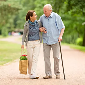 Elderly man walking with cane walking with caregiver. 